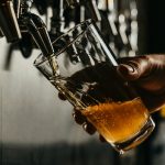 person pouring brown liquid on clear drinking glass